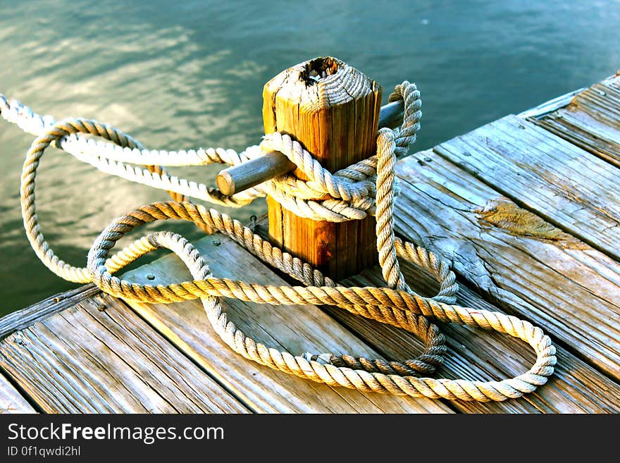 Boat (not shown) moored to post on wooden jetty with spare rope twisted loosely around. Boat (not shown) moored to post on wooden jetty with spare rope twisted loosely around.