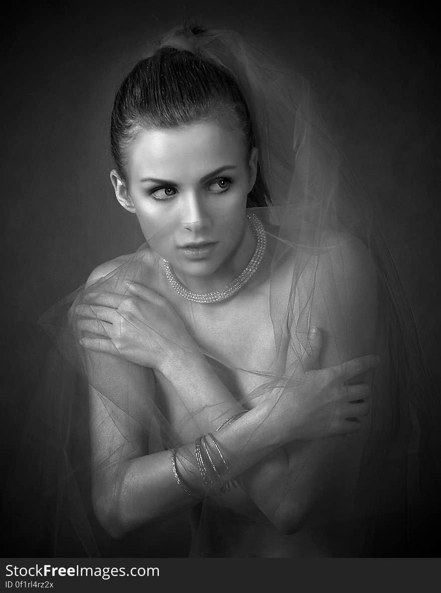 A black and white portrait of a young woman with a necklace and a bracelet hugging herself. A black and white portrait of a young woman with a necklace and a bracelet hugging herself.