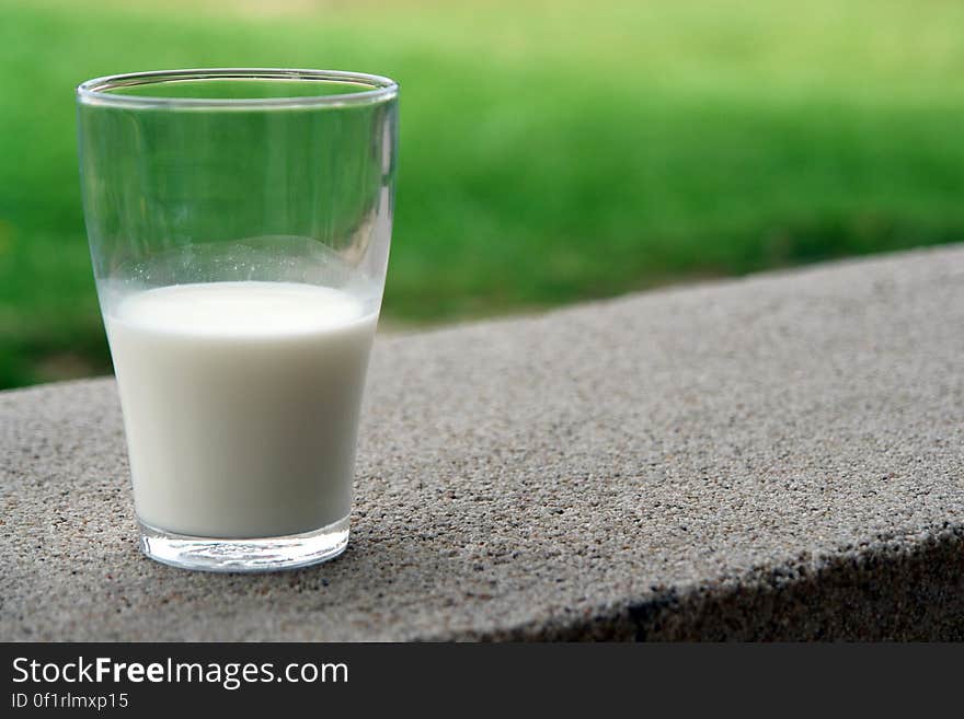 A close up of a glass of milk on a concrete surface outdoor.