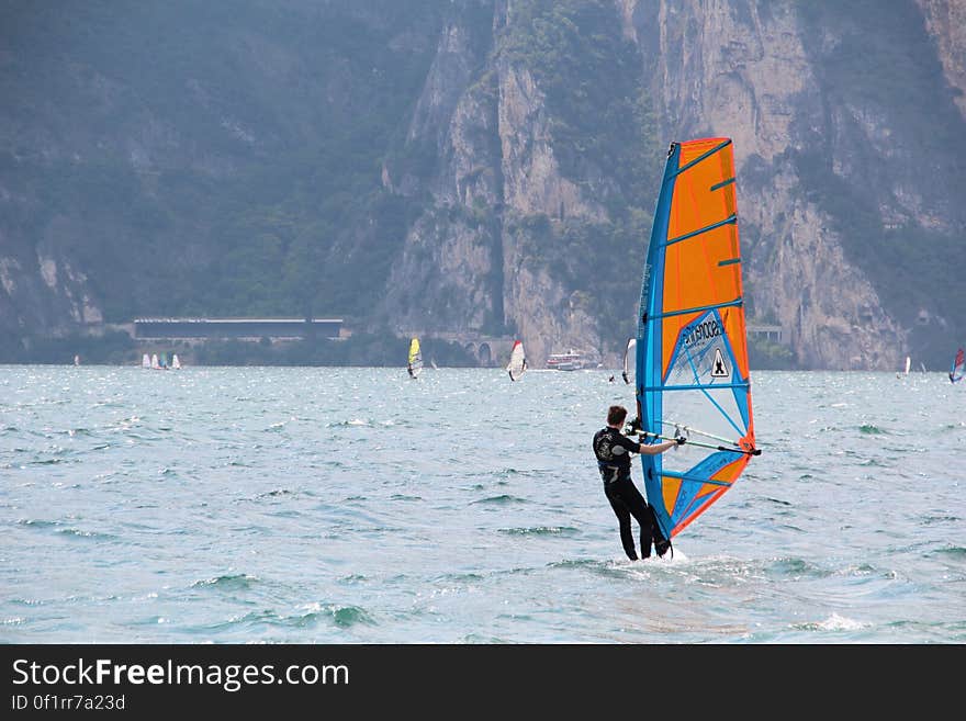 Man in Black Wetsuit Standing on Orange and Blue Sailboat during Daytime