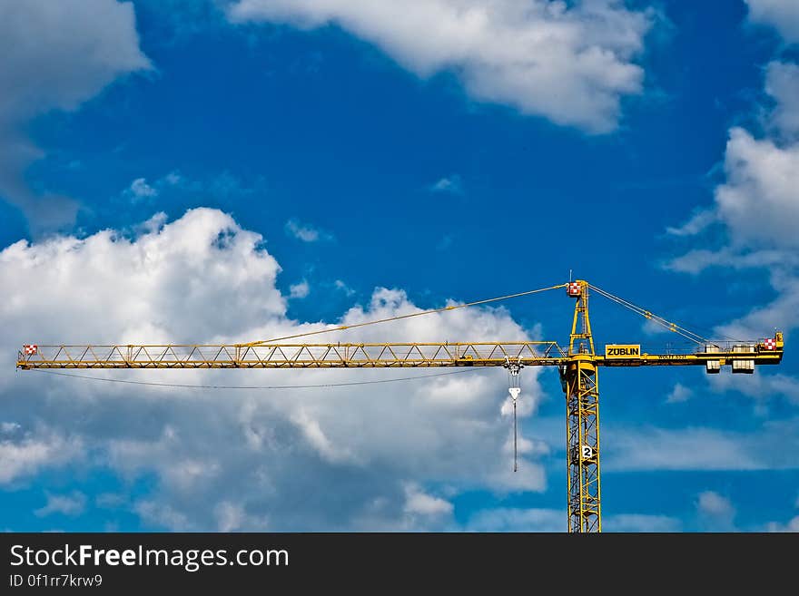 Upper parts of computerized crane with supporting cables and main steel column seen against blue sky and fluffy white clouds. Upper parts of computerized crane with supporting cables and main steel column seen against blue sky and fluffy white clouds.