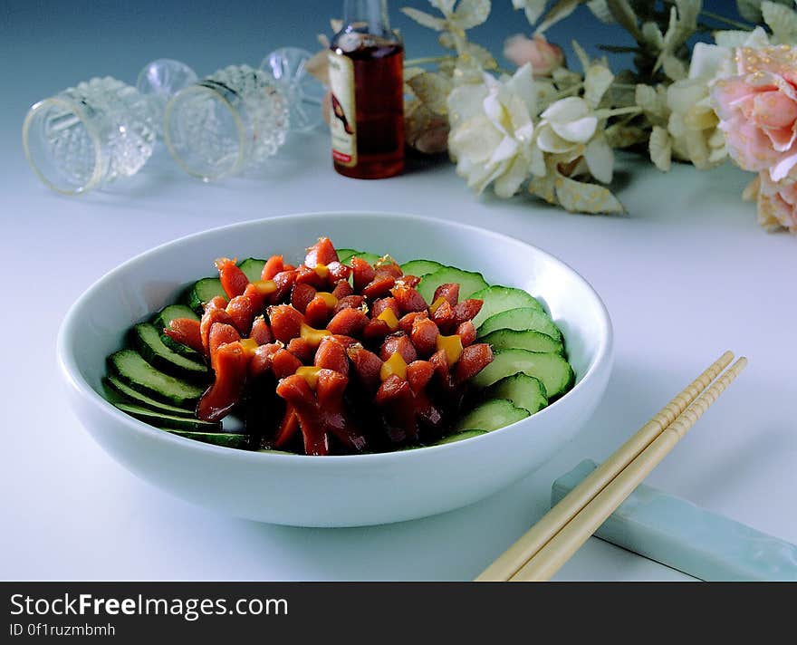 A bowl of salad on table with chopsticks and floral arrangement. A bowl of salad on table with chopsticks and floral arrangement.