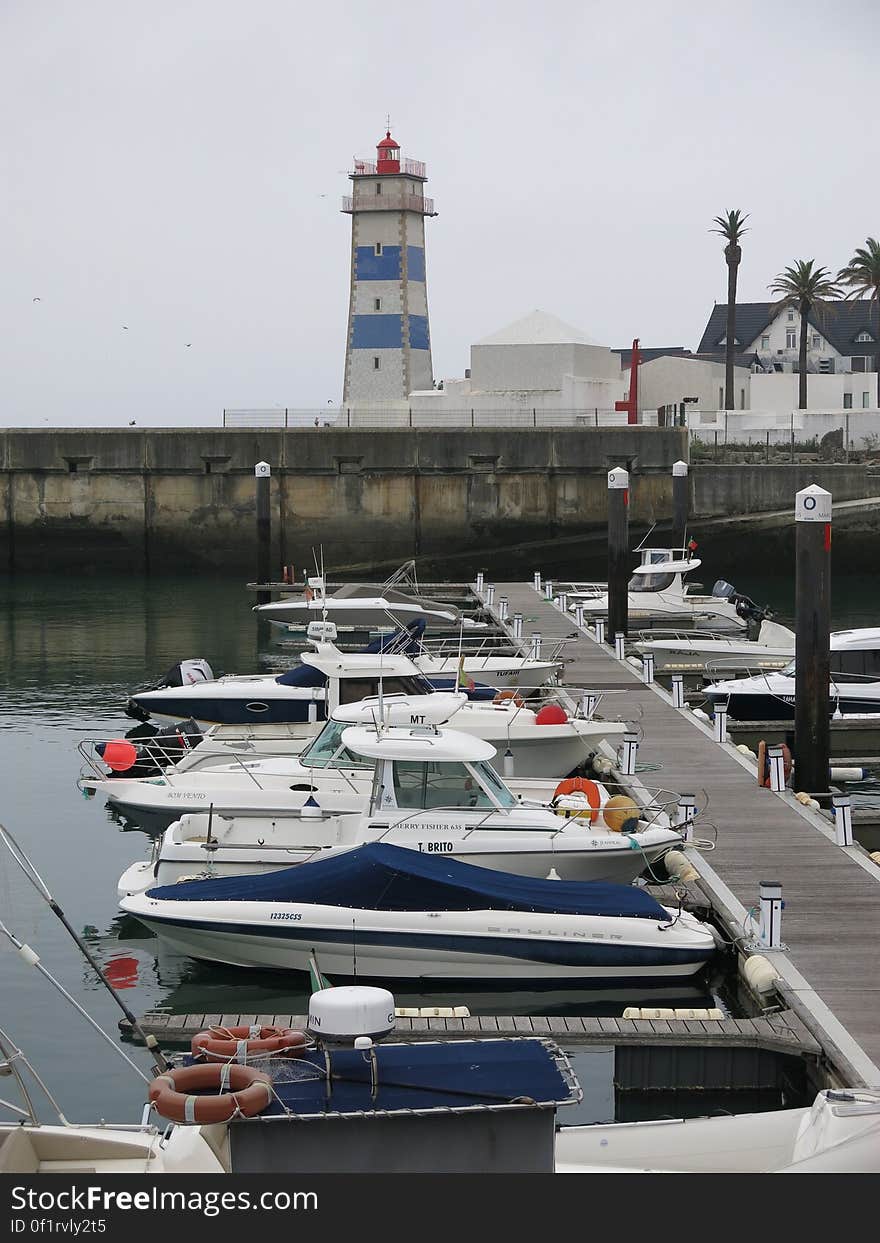 Lighthouse on seawall with boats along dock on waterfront. Lighthouse on seawall with boats along dock on waterfront.