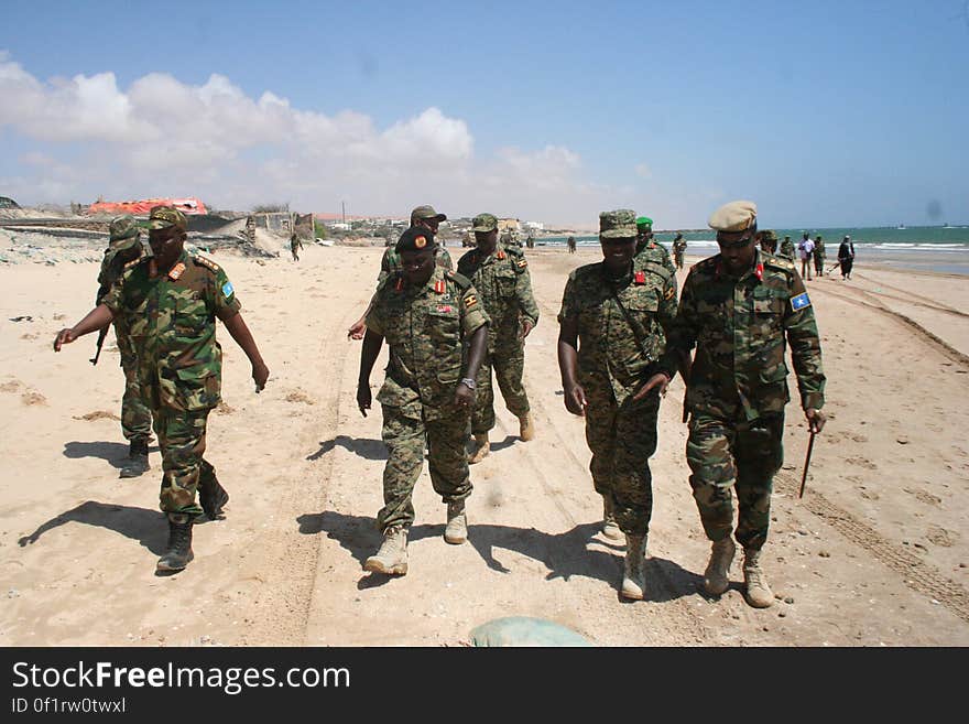 Soldiers in uniform walking on sandy beach on sunny day. Soldiers in uniform walking on sandy beach on sunny day.