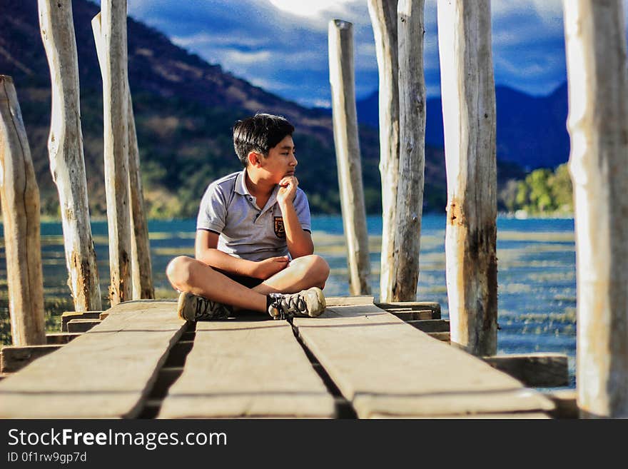 Young boy sitting in shorts on edge of wooden pier on sunny day. Young boy sitting in shorts on edge of wooden pier on sunny day.