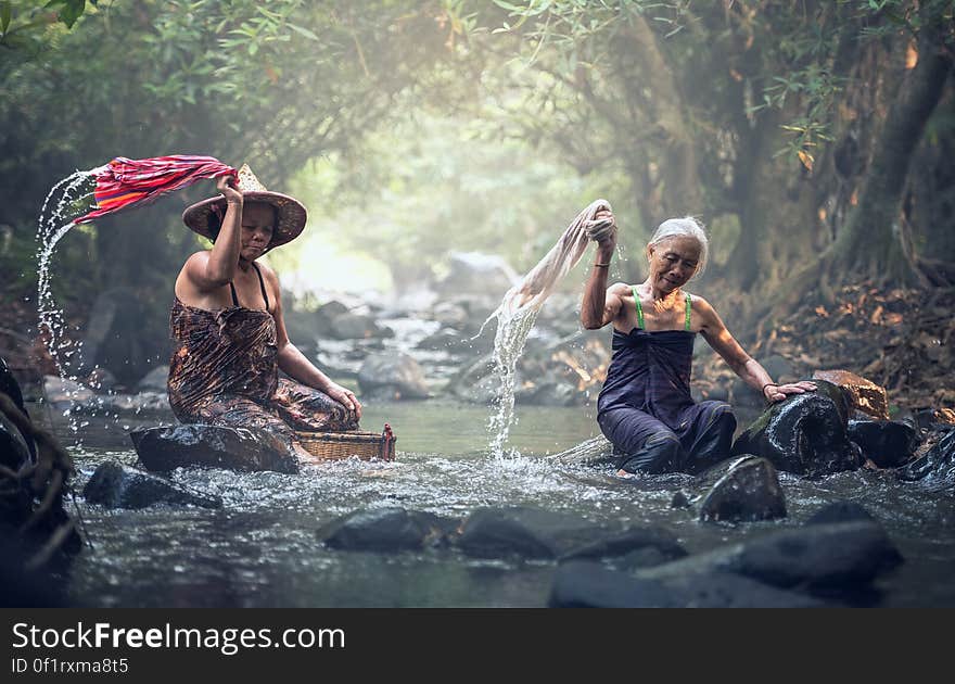 A couple of Asian women washing clothes in the river.