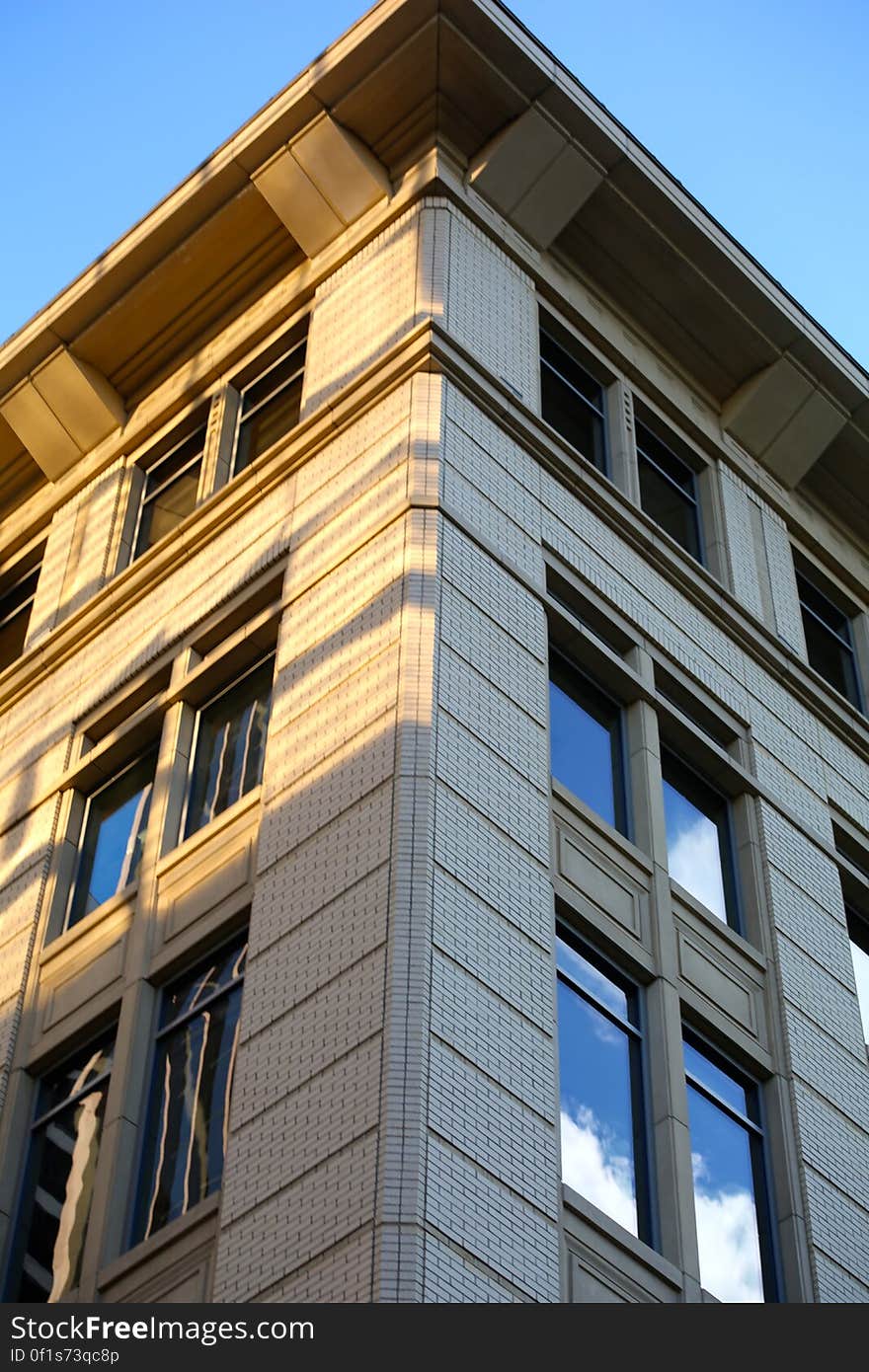 Corner of modern architect designed office building constructed of gray brick and glass with eaves and soffit visible, blue sky and cloud reflected in the glass. Corner of modern architect designed office building constructed of gray brick and glass with eaves and soffit visible, blue sky and cloud reflected in the glass.