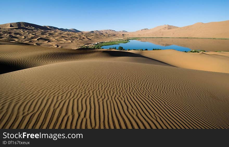 Landscape of ridged desert sands and blue lake dunes extending into the far distance, cloudless blue sky background. Landscape of ridged desert sands and blue lake dunes extending into the far distance, cloudless blue sky background.