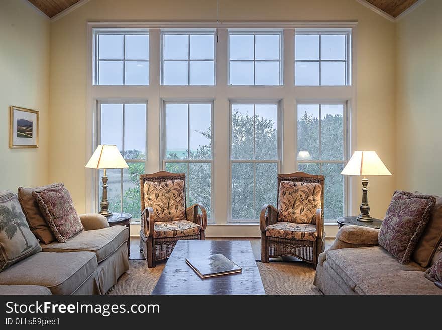 Sitting room in modern apartment with large windows looking onto the garden, vaulted ceiling and with two settees and two arm chairs, coffee table and reading lamps.