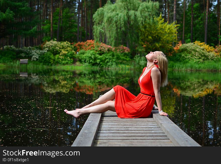 Beautiful woman in red dress sat on pier relaxing by lake in countryside. Beautiful woman in red dress sat on pier relaxing by lake in countryside.