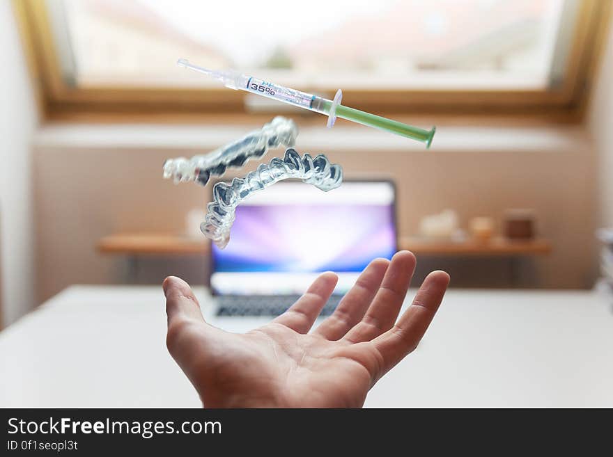 A close up of a hand catching falling denture and syringe and a laptop in the background.