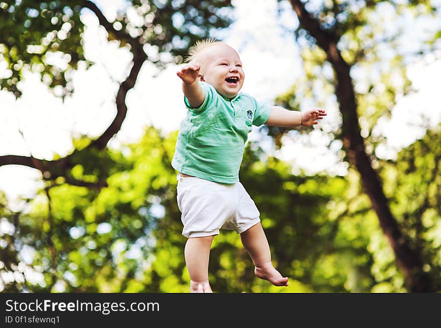 Happy young baby boy jumping in midair with trees in background.