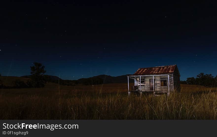 Abandoned barn in countryside at night with starry sky.
