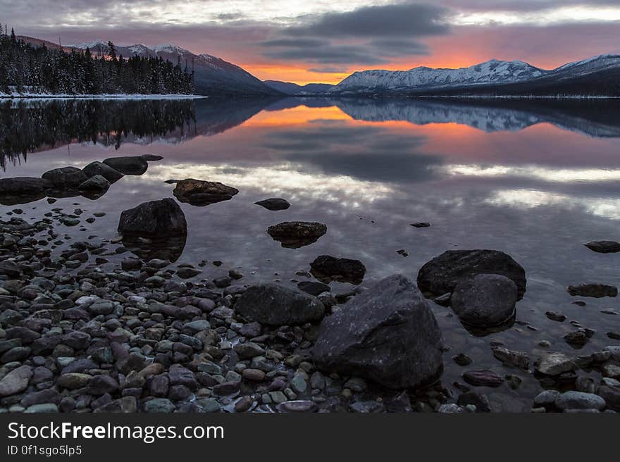 Cloud reflecting on lake at sunset with snow capped mountains in distance.