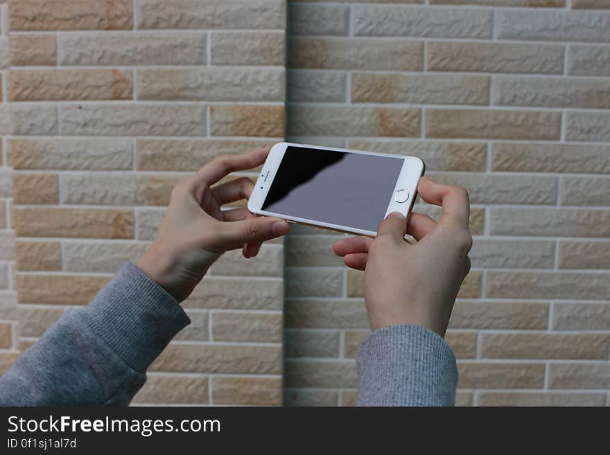 Two adult hands holding a smart phone against a brick background. Two adult hands holding a smart phone against a brick background.