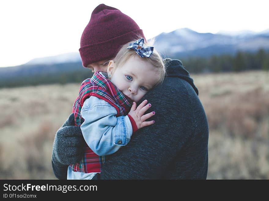 Father in maroon tea cozy hat carrying smiling baby daughter wearing blue shirt and tartan jacket on his shoulder, background of distant snowy mountains. Father in maroon tea cozy hat carrying smiling baby daughter wearing blue shirt and tartan jacket on his shoulder, background of distant snowy mountains.