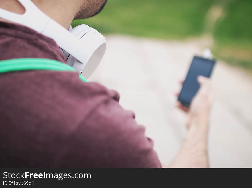 A man with headphones around his neck looking at smartphone.