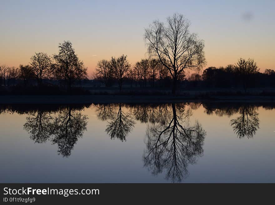 Reflection of Silhouette Trees in Lake Against Sky at Sunset