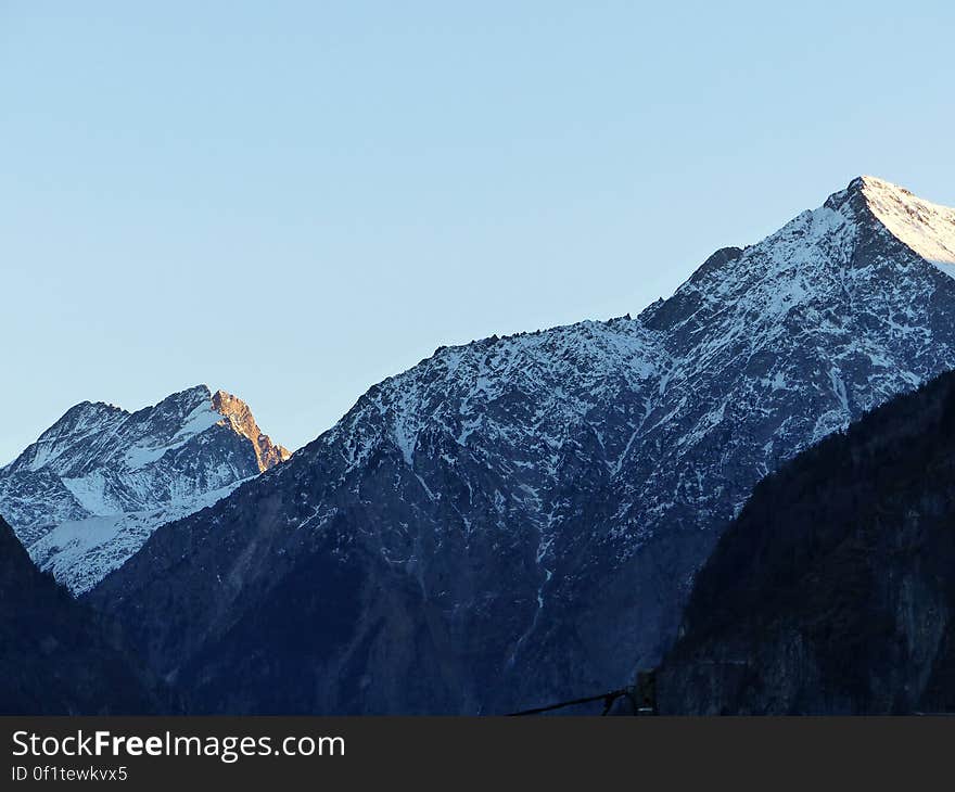 Peaks of snow capped mountain range with blue sky background.