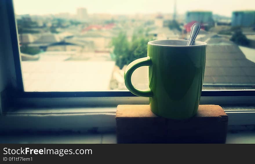 Cup of coffee on house window sill with city buildings in background.