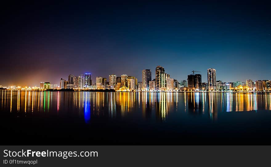 Modern city skyline at night reflected on calm sea or ocean. Modern city skyline at night reflected on calm sea or ocean.