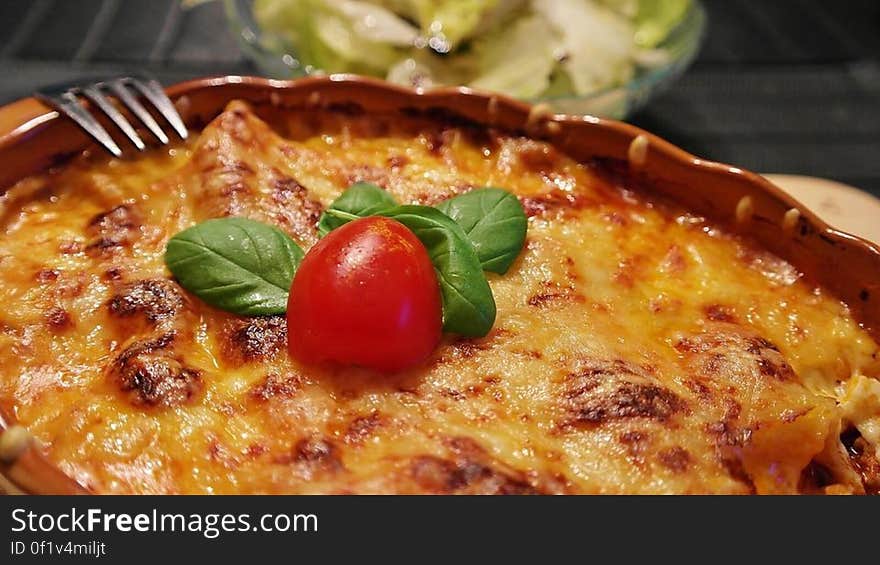 Close up of tomato and basil on top of cheesy casserole in dish with fork.