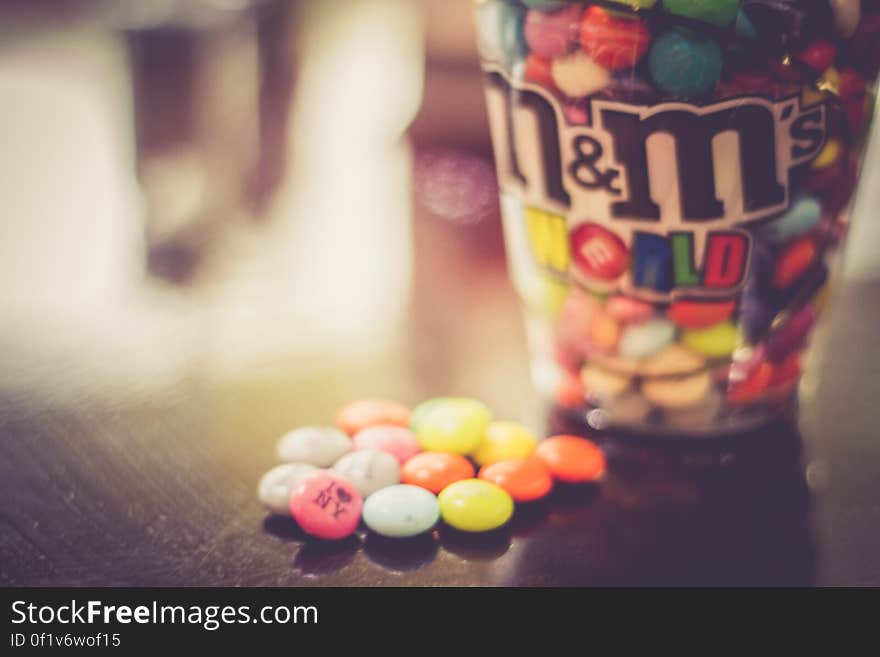 Close up of cup of M&M candies on wooden table.