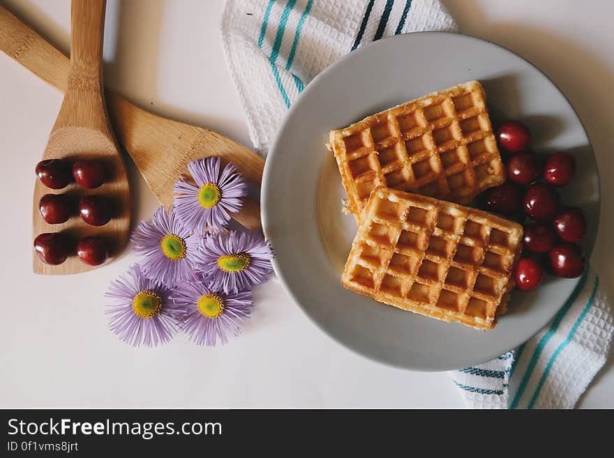 Overhead view of plate of cooked waffles on table with fresh cherries and flowers. Overhead view of plate of cooked waffles on table with fresh cherries and flowers.