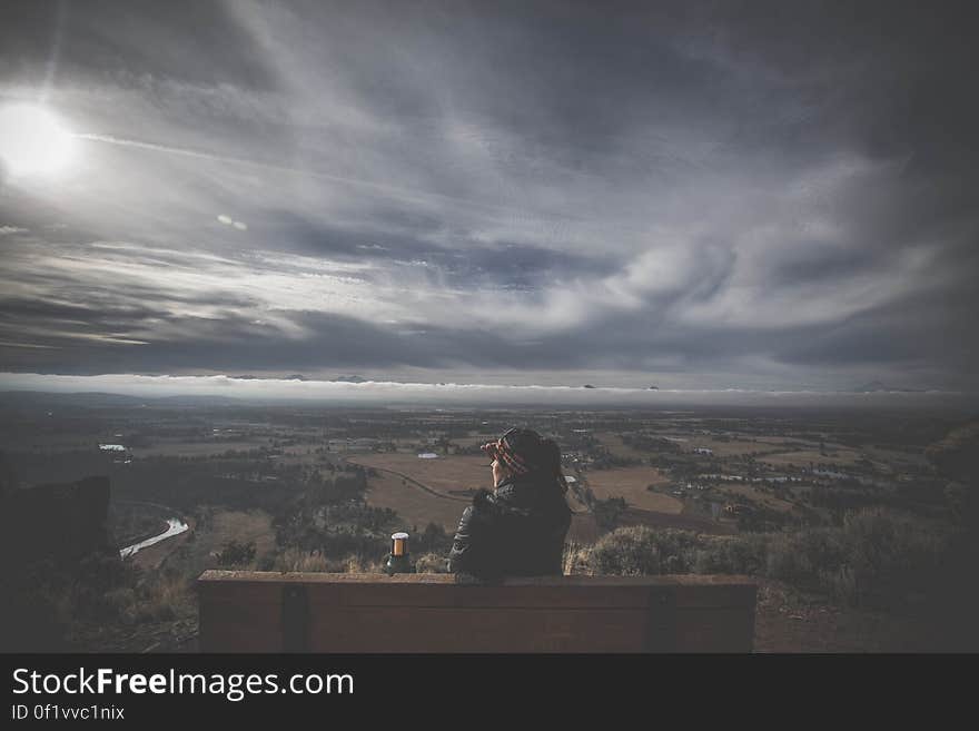 Rear view of woman sat on bench on hill looking over countryside with cloudscape background and sun flare. Rear view of woman sat on bench on hill looking over countryside with cloudscape background and sun flare.