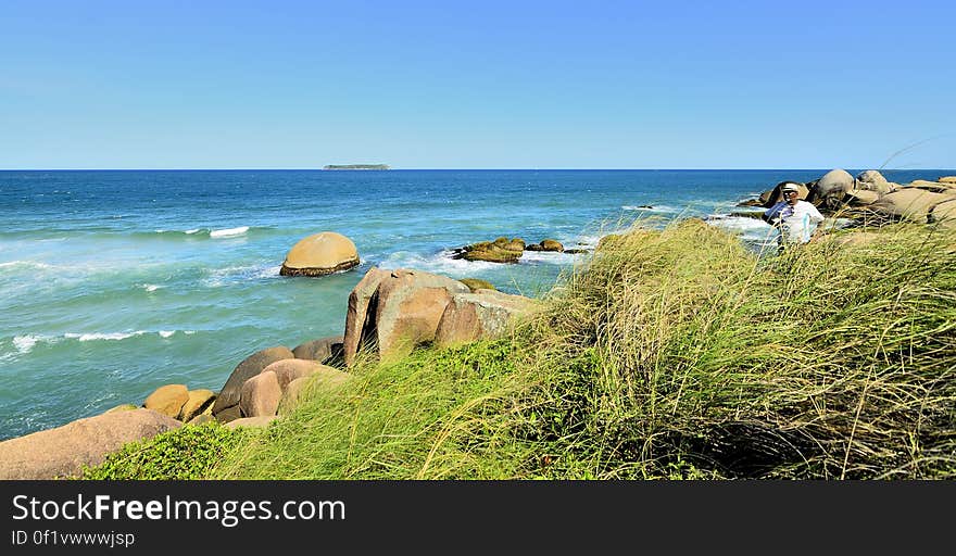 Person standing on rocky coastline on sunny day.