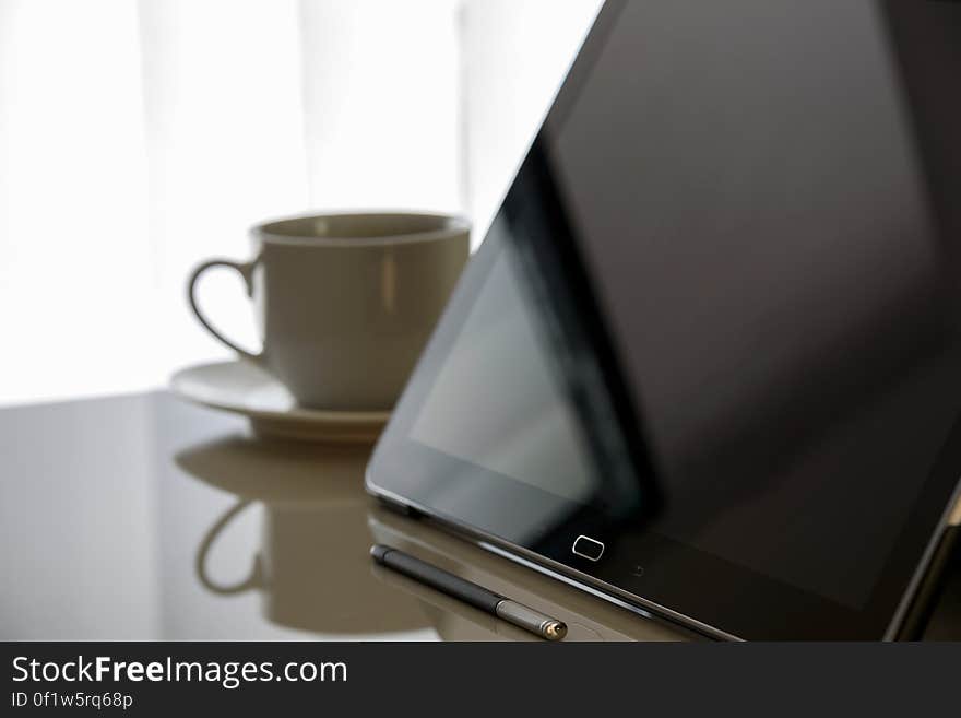 Closeup of tablet, pen and cup of coffee on a reflective surface with selective focus, white background.