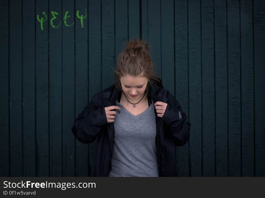 Smart young woman looking down while adjusting the black jacket over her gray knitted dress, dark painted wooden background. Smart young woman looking down while adjusting the black jacket over her gray knitted dress, dark painted wooden background.