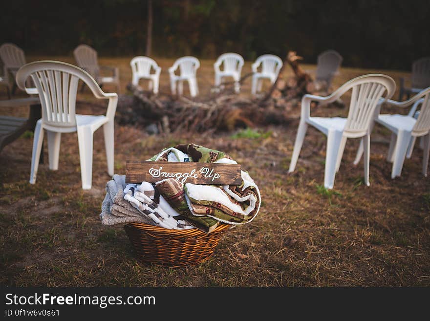 A fire pit with plastic chairs around it and a basket of blankets. A fire pit with plastic chairs around it and a basket of blankets.