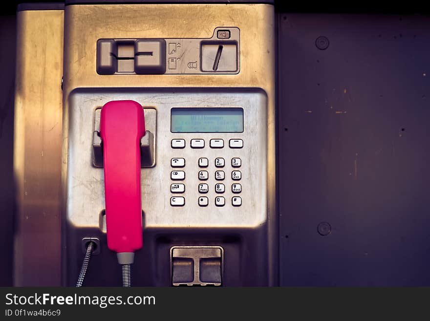 Closeup of a public pay phone with a red handset and silver button keypad. Closeup of a public pay phone with a red handset and silver button keypad.