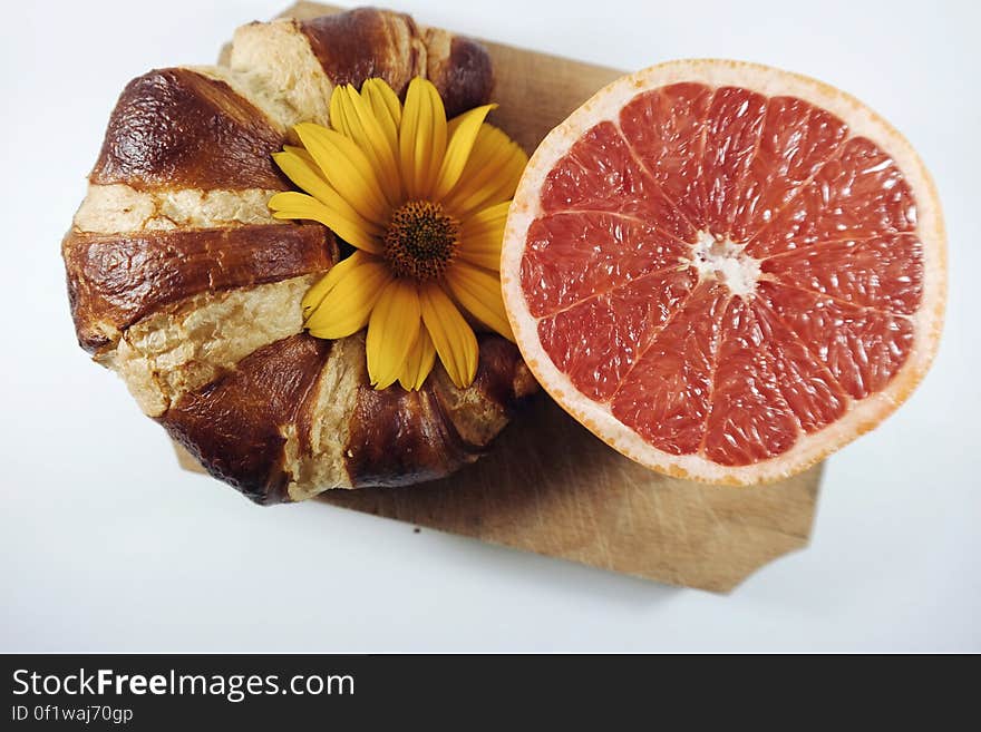 A croissant and a half of red grapefruit decorated with a yellow flower. A croissant and a half of red grapefruit decorated with a yellow flower.