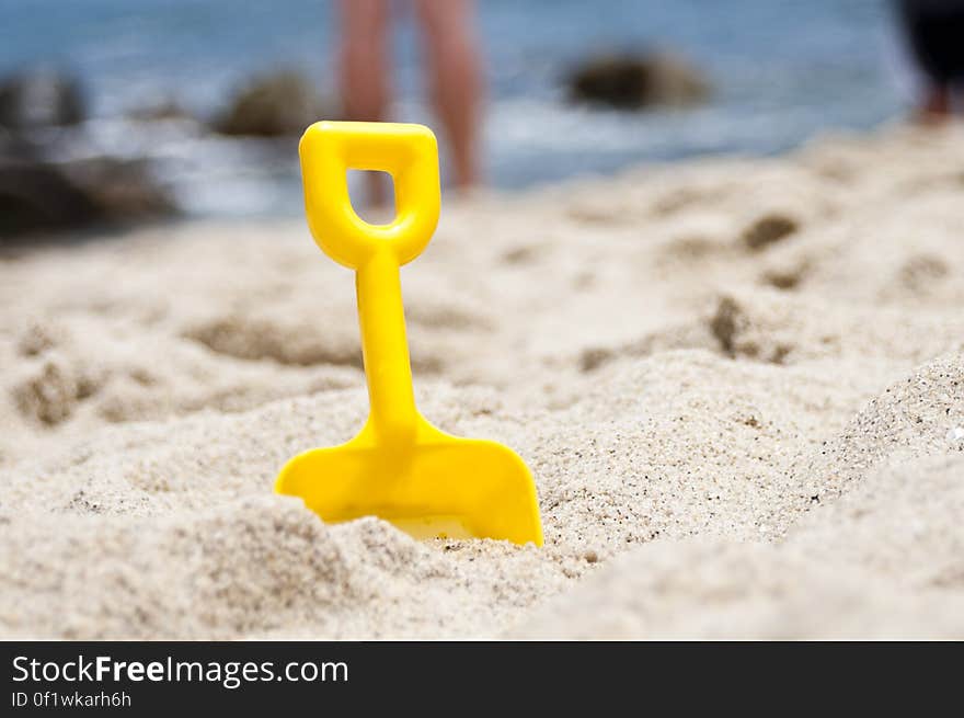 Closeup of a yellow plastic spade on the beach symbol of Summer holidays at the seaside background of sea and sky.