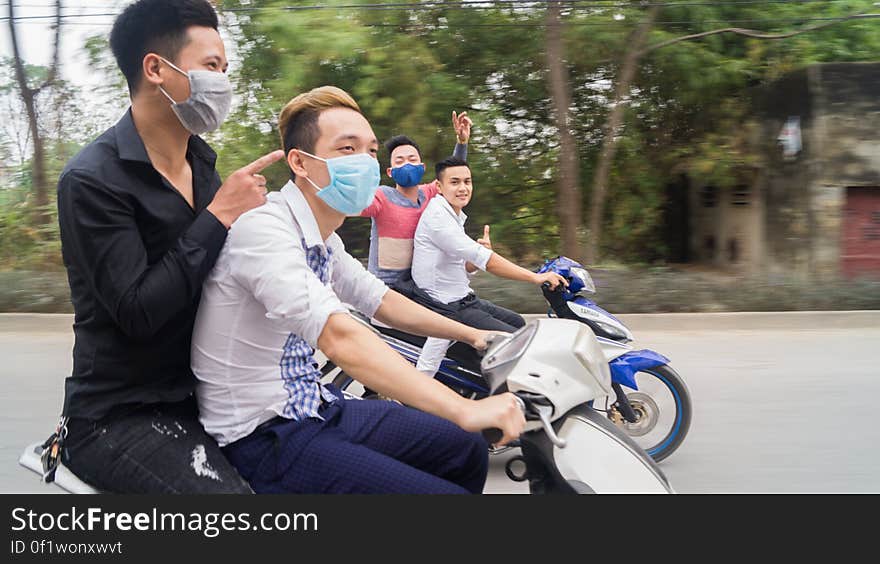 Asian men wearing face masks riding motor scooters on street. Asian men wearing face masks riding motor scooters on street.