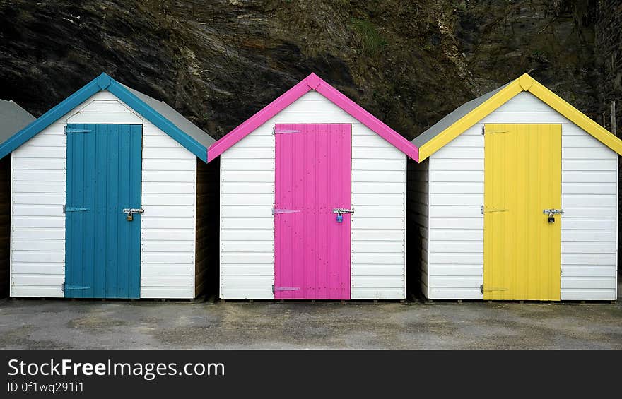 Colorful bathing huts in white but with blue, pink (mauve) and yellow doors situated at the bottom of a cliff. Colorful bathing huts in white but with blue, pink (mauve) and yellow doors situated at the bottom of a cliff.