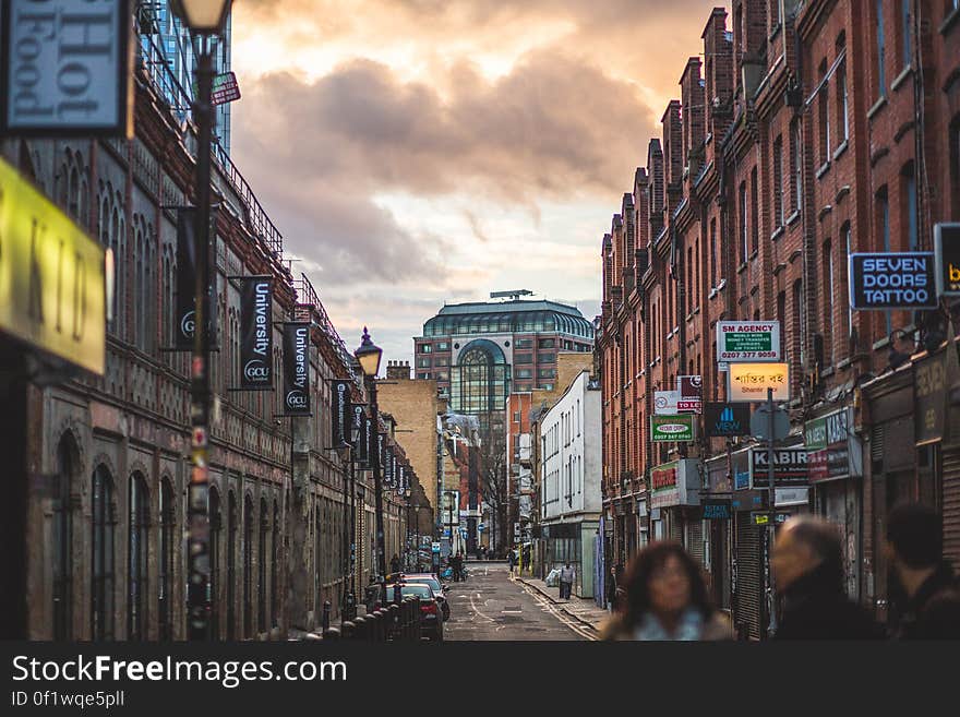 Person on Road Between Brown Walled Building during Daytime Under Cumulus Clouds