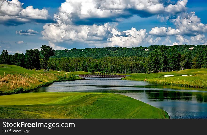 A river running through a green, rolling golf course with fluffy, white clouds in a blue sky. A river running through a green, rolling golf course with fluffy, white clouds in a blue sky.