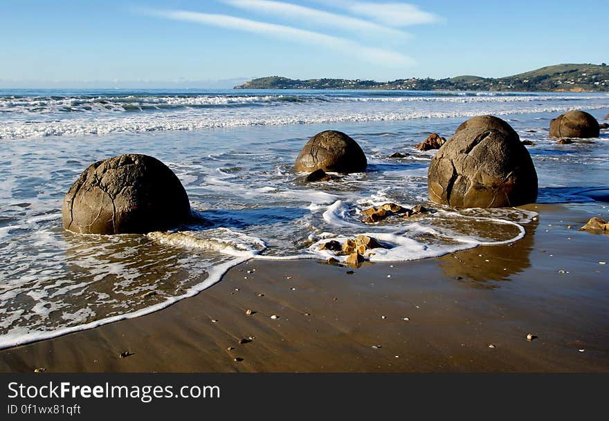 The Moeraki Boulders are unusually large and spherical boulders lying along a stretch of Koekohe Beach on the wave cut Otago coast of New Zealand between Moeraki and Hampden. They occur scattered either as isolated or clusters of boulders within a stretch of beach where they have been protected in a scientific reserve. The erosion by wave action of mudstone, comprising local bedrock and landslides, frequently exposes embedded isolated boulders. These boulders are grey-colored septarian concretions, which have been exhumed from the mudstone enclosing them and concentrated on the beach by coastal erosion. The Moeraki Boulders are unusually large and spherical boulders lying along a stretch of Koekohe Beach on the wave cut Otago coast of New Zealand between Moeraki and Hampden. They occur scattered either as isolated or clusters of boulders within a stretch of beach where they have been protected in a scientific reserve. The erosion by wave action of mudstone, comprising local bedrock and landslides, frequently exposes embedded isolated boulders. These boulders are grey-colored septarian concretions, which have been exhumed from the mudstone enclosing them and concentrated on the beach by coastal erosion