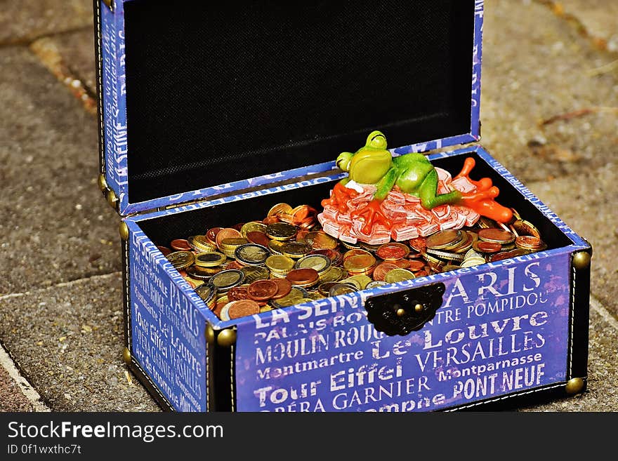 A blue decorative chest filled with coins and a frog figurine.