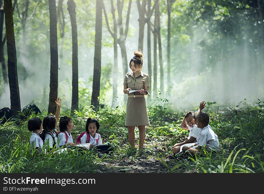 Woman in Gray Long Sleeve Dress Standing Between Childrens Near Woods and Grass