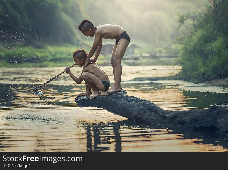 A pair of young Asian boys spear fishing on a river. A pair of young Asian boys spear fishing on a river.