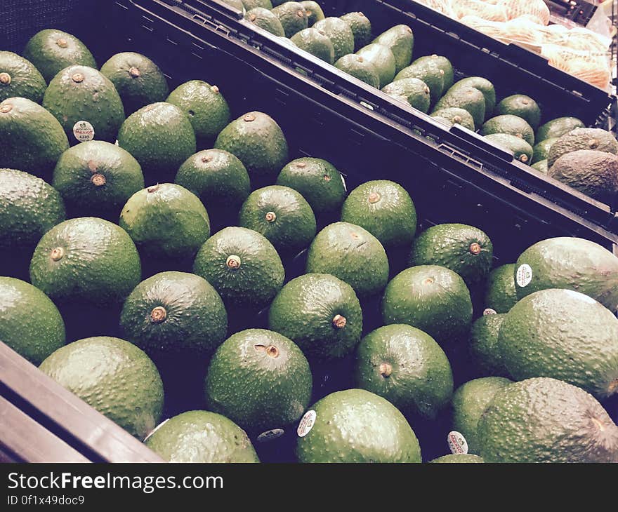 A shop vegetable and fruit area with trays of green avocado fruits. A shop vegetable and fruit area with trays of green avocado fruits.