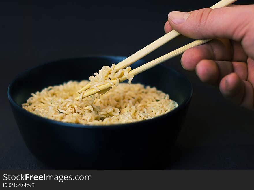 Person Holding a Chopsticks and Picking a Noodles in Black Bowl