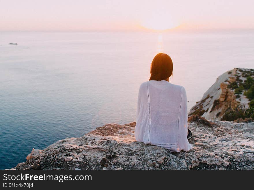 A woman sitting on a rock at the seaside watching the sun near the horizon. A woman sitting on a rock at the seaside watching the sun near the horizon.