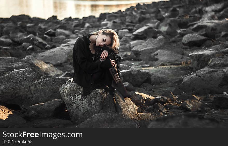 A woman sitting on the rocks of a rocky shore. A woman sitting on the rocks of a rocky shore.