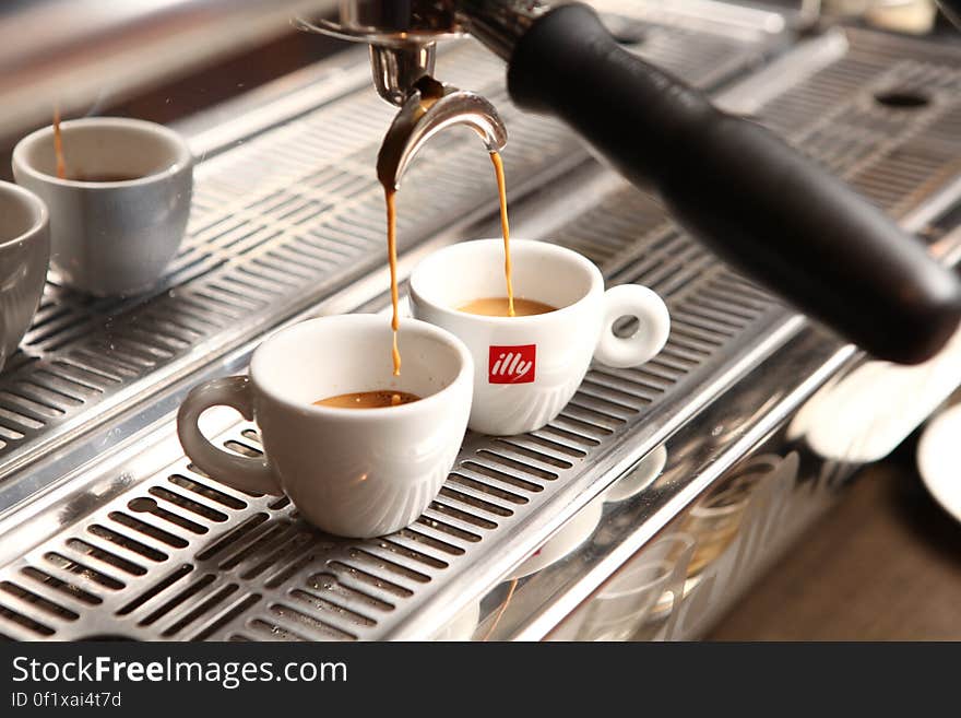 Two cups below an espresso machine being filled with espresso. Two cups below an espresso machine being filled with espresso.