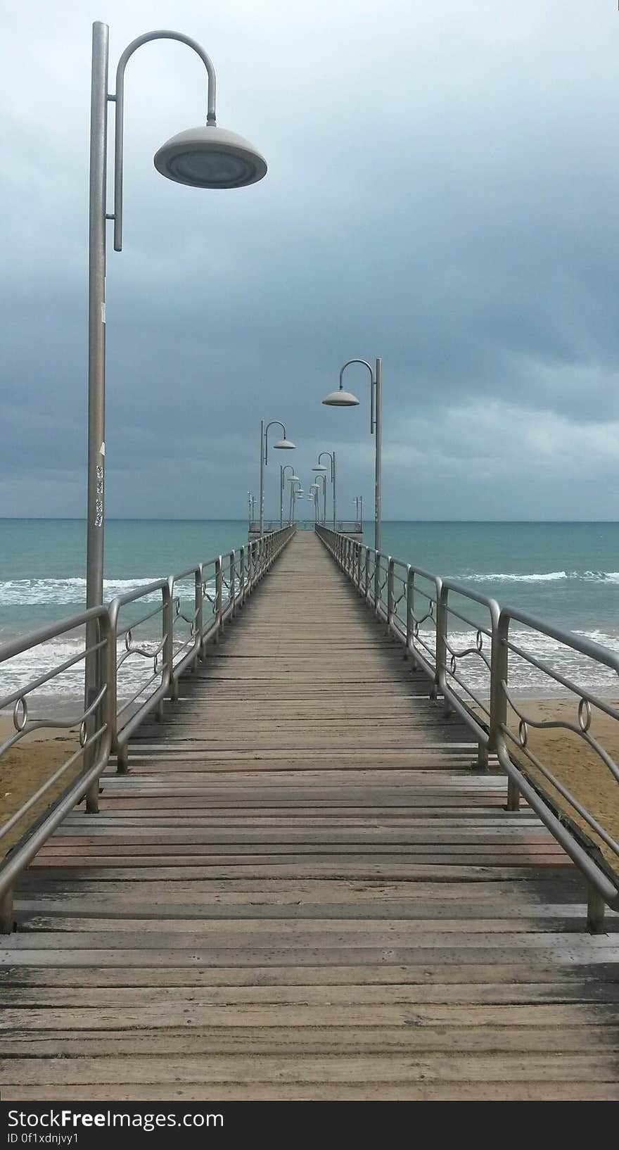 A boardwalk with lamps and metal railing across a sandy beach, open sea in the background. A boardwalk with lamps and metal railing across a sandy beach, open sea in the background.